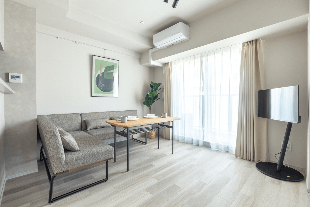 Modern living room with a gray L-shaped sofa, light wood table, large window, and mounted TV.