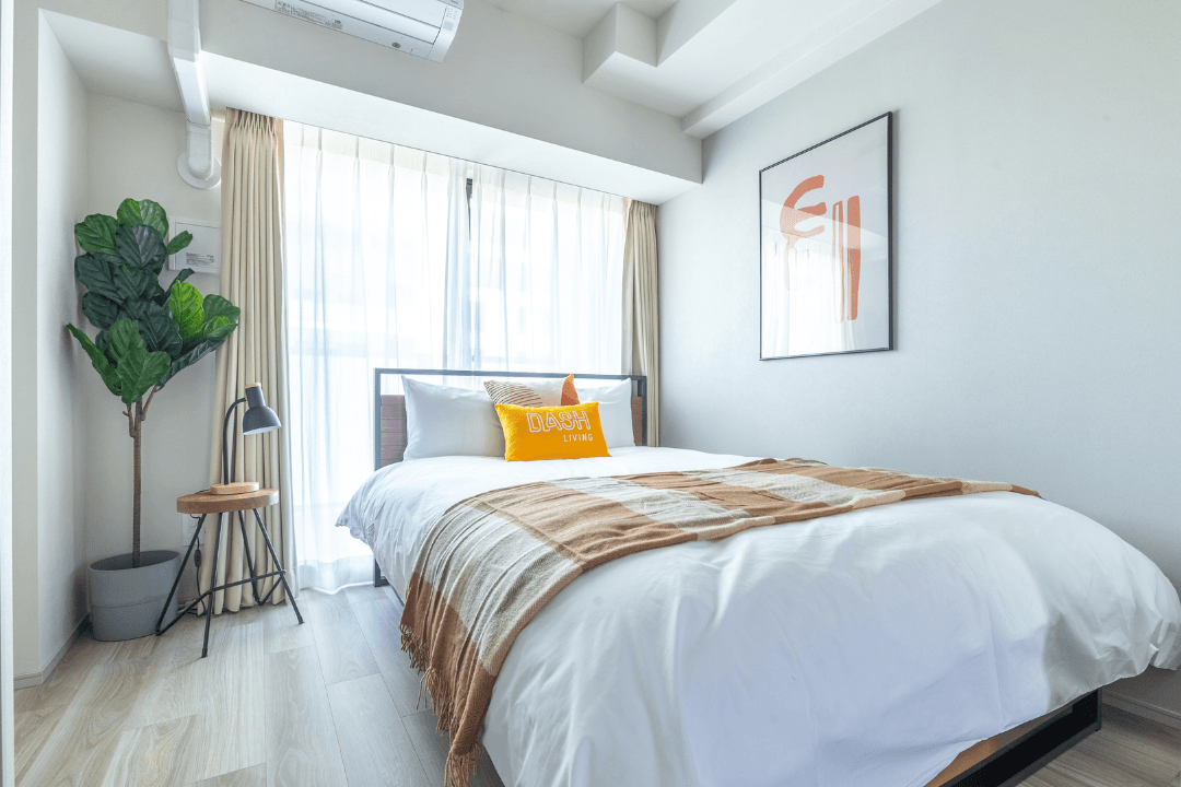 A modern bedroom with a white bed, fiddle-leaf fig plant, and abstract art.
