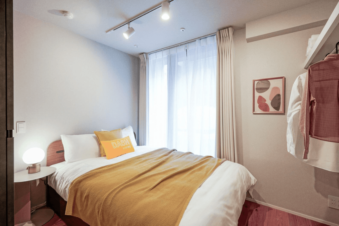 Modern bedroom with a neatly made bed, nightstand, lamp, and window.