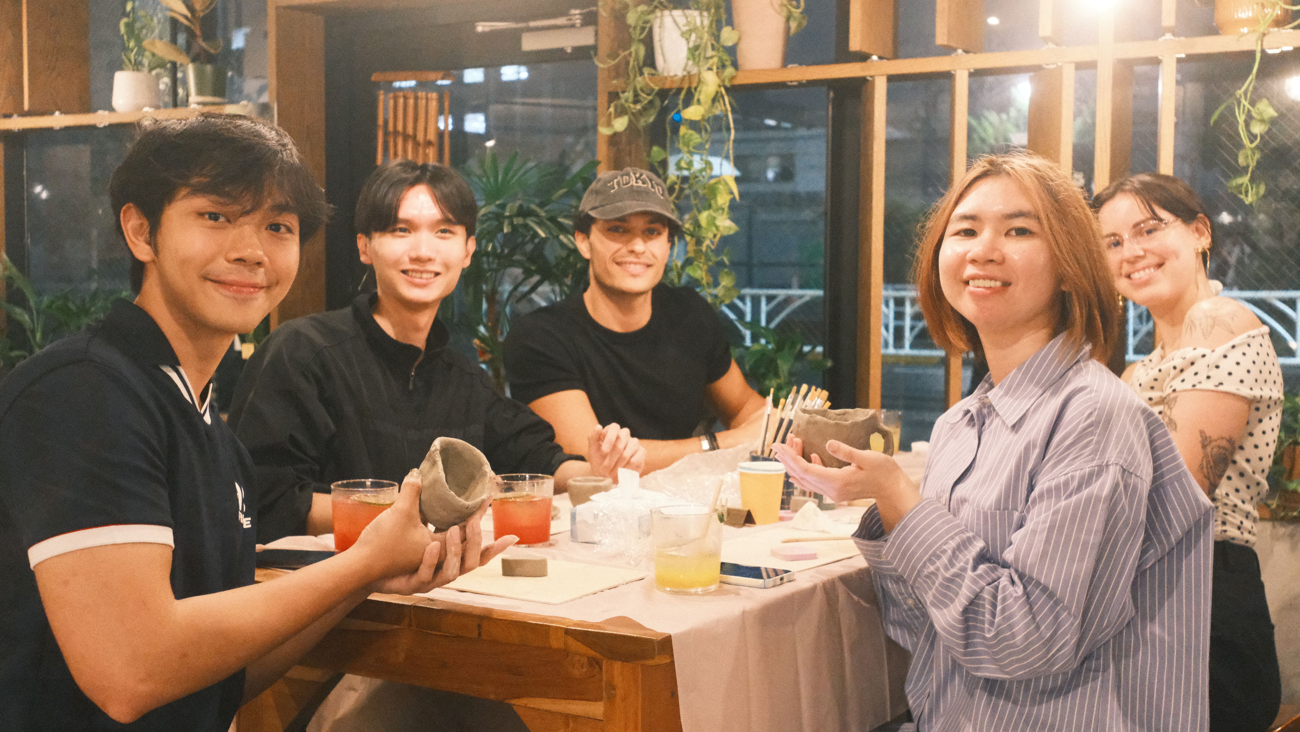 Five friends are smiling at a restaurant table with drinks and plates.