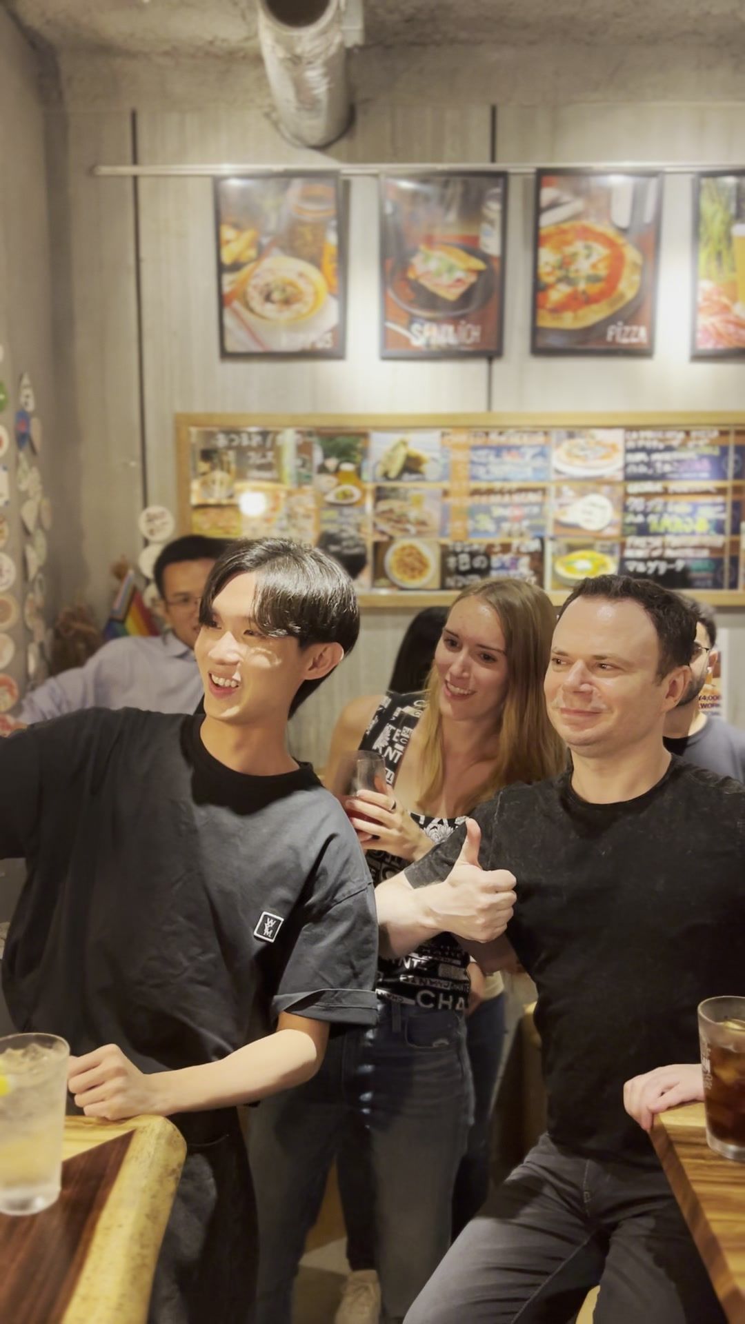 Three friends smiling and looking left in a lively restaurant with framed art.