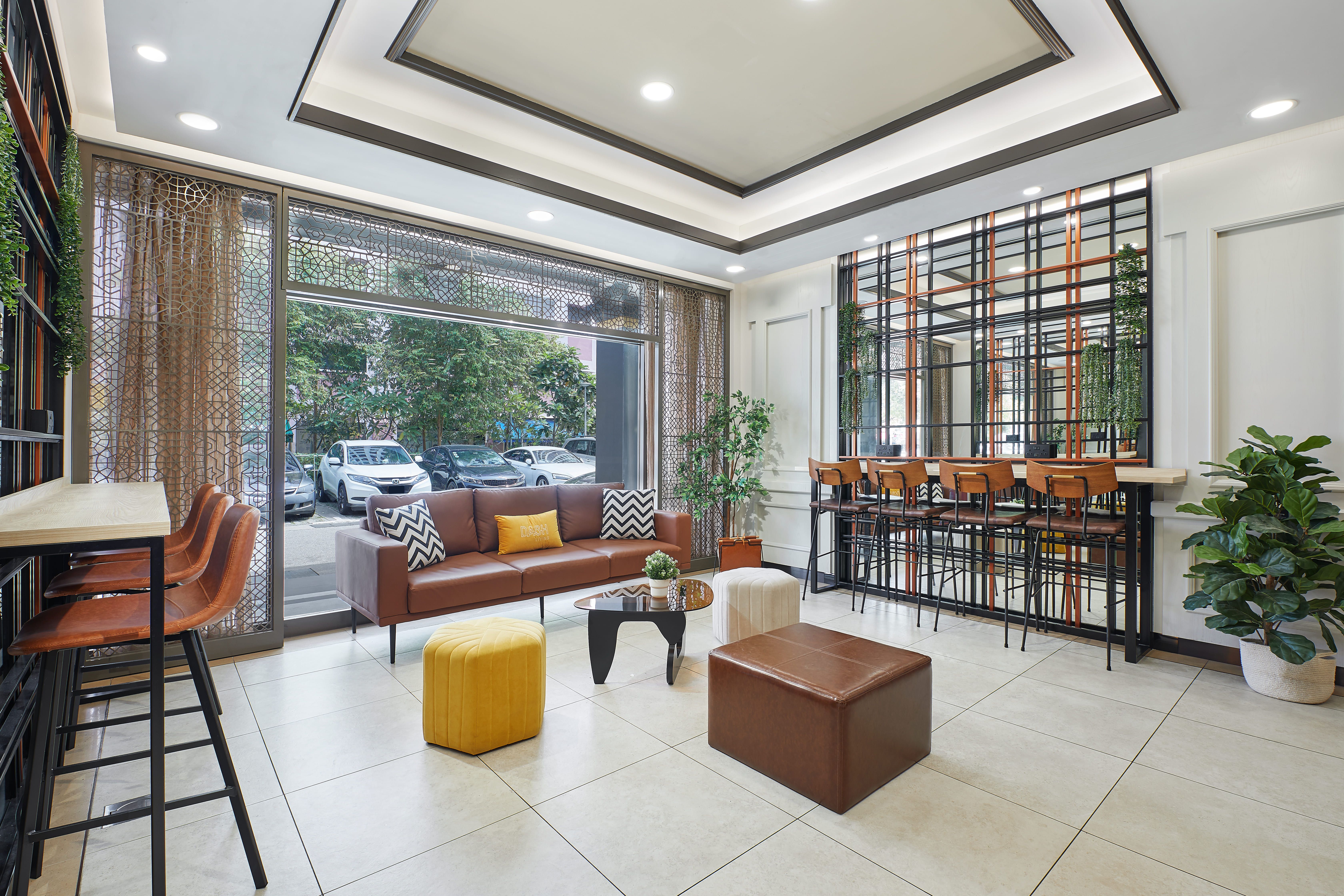 Bright, modern lounge with leather sofa, bar seating, large windows, and green plants.