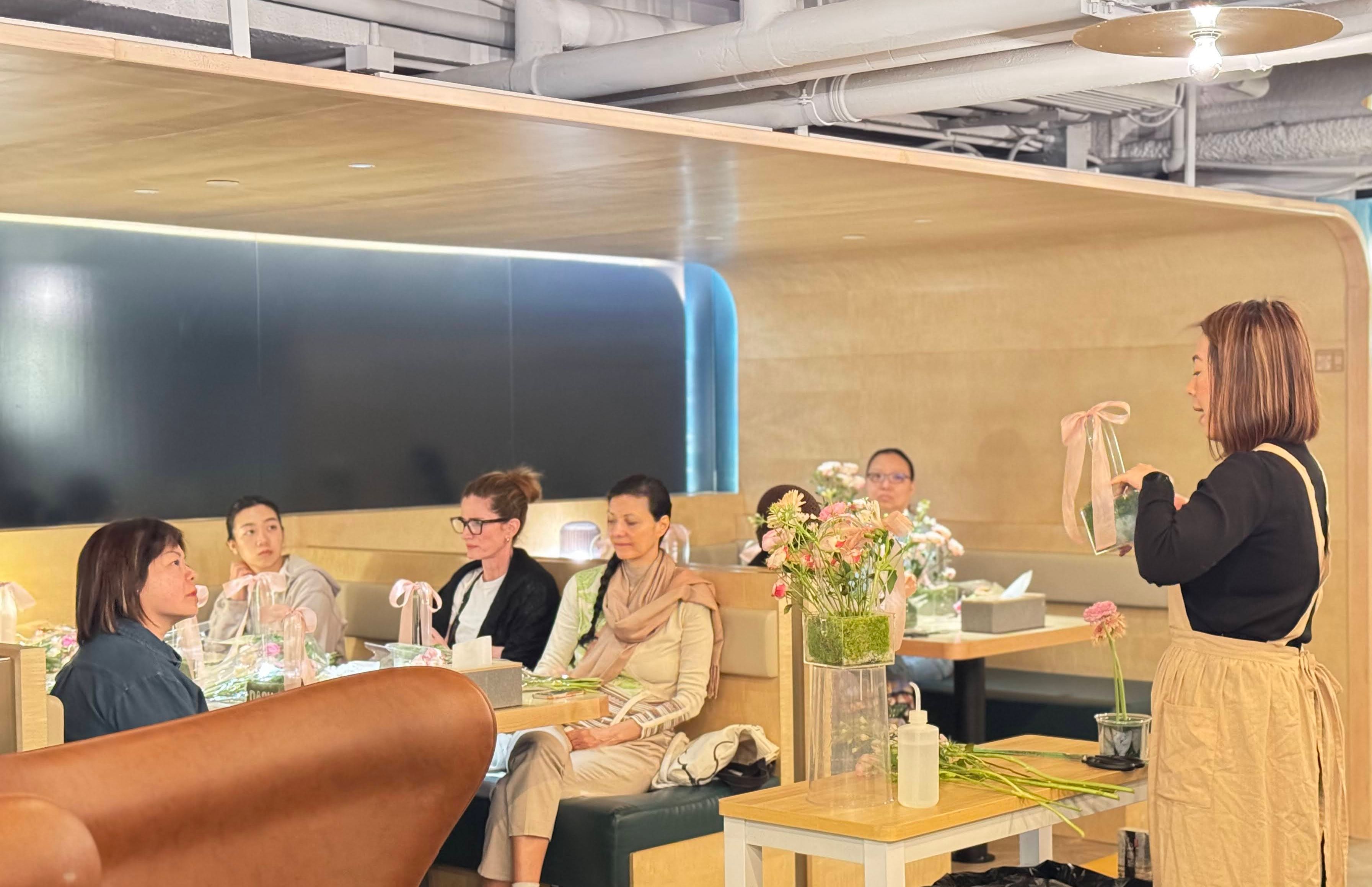 Woman leading a floral workshop for seated participants in a modern bright interior.