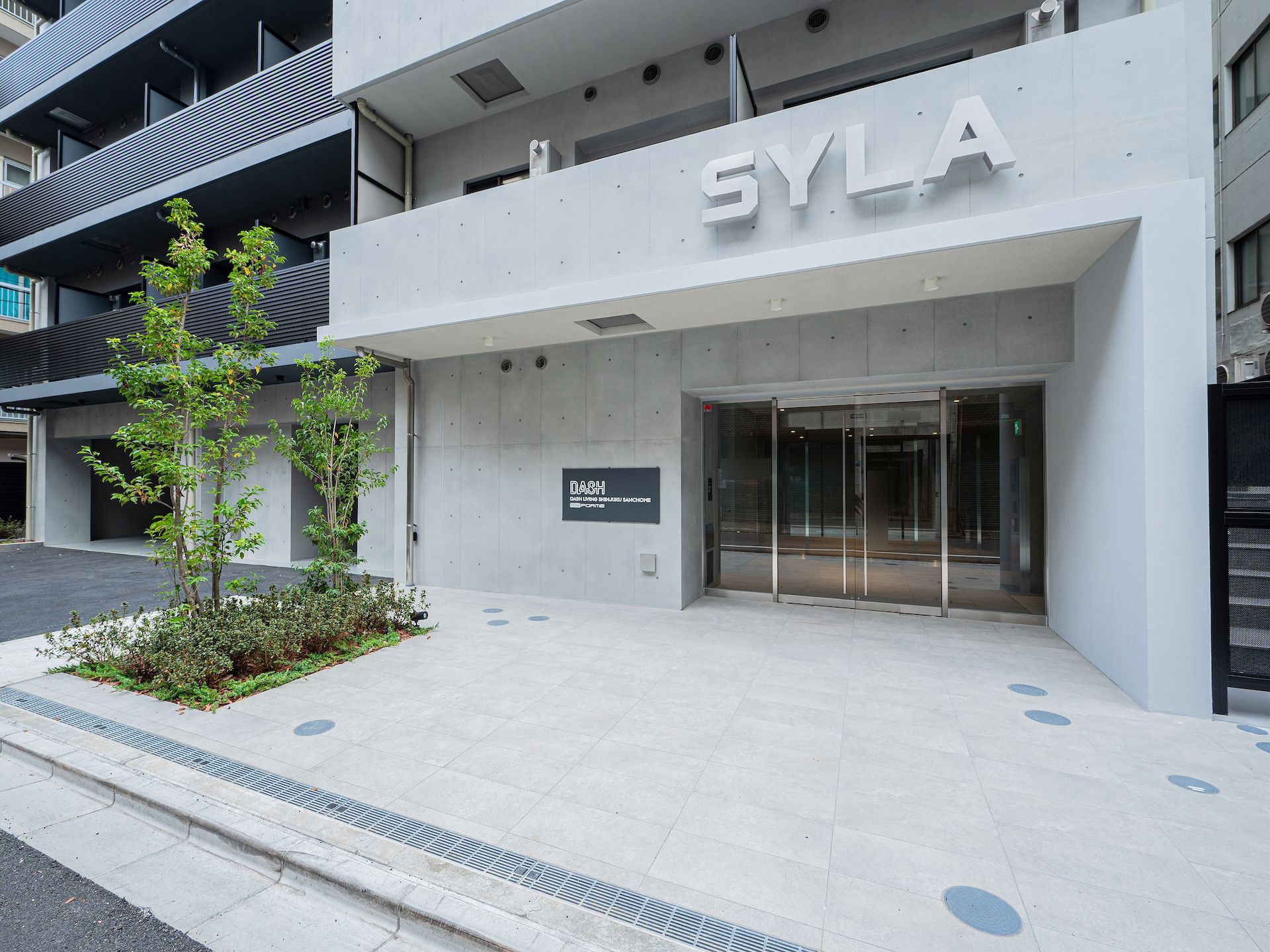Modern building entrance with 'SYLA' sign above glass doors and small green landscaping.