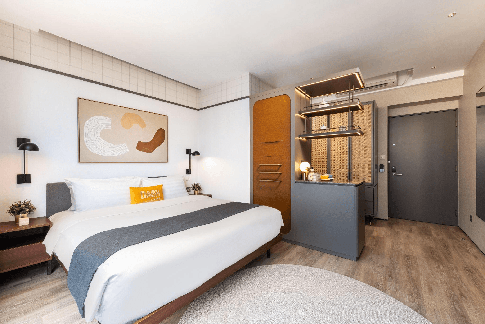 Modern hotel room with a large bed, abstract art, and a compact kitchenette.