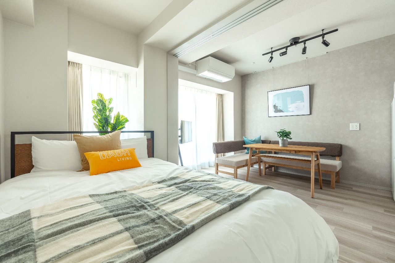 Bright, modern studio apartment with a comfortable bed, dining area, and natural light.