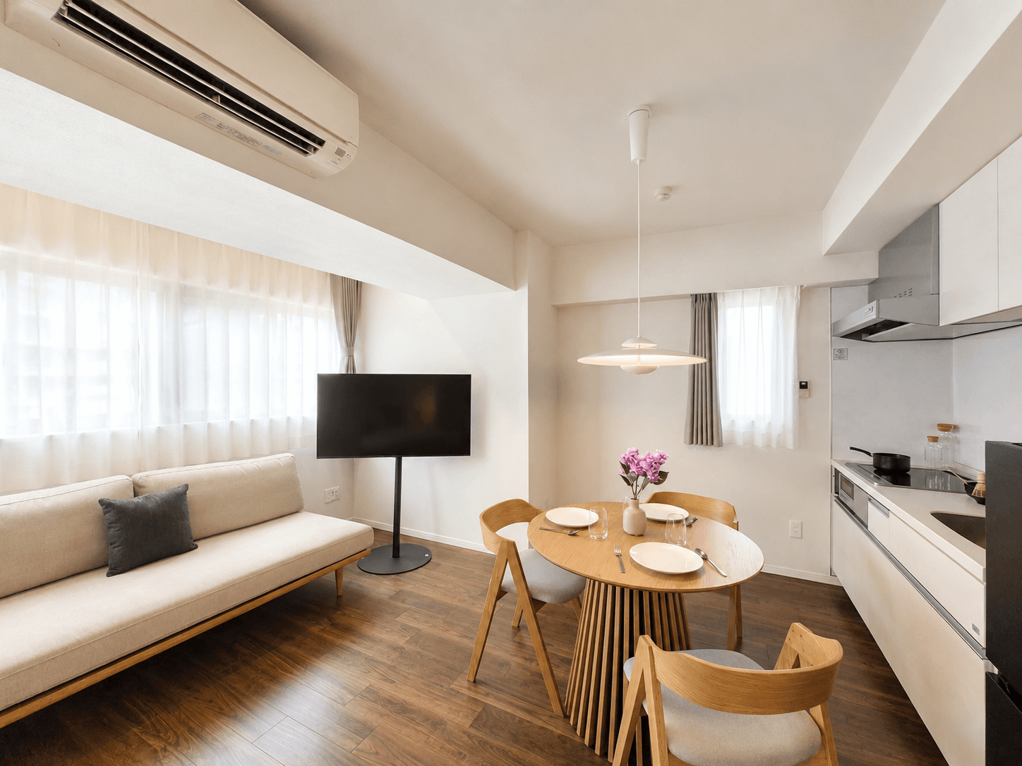 Bright, modern open-plan living area with a sofa, dining table, and compact kitchen.