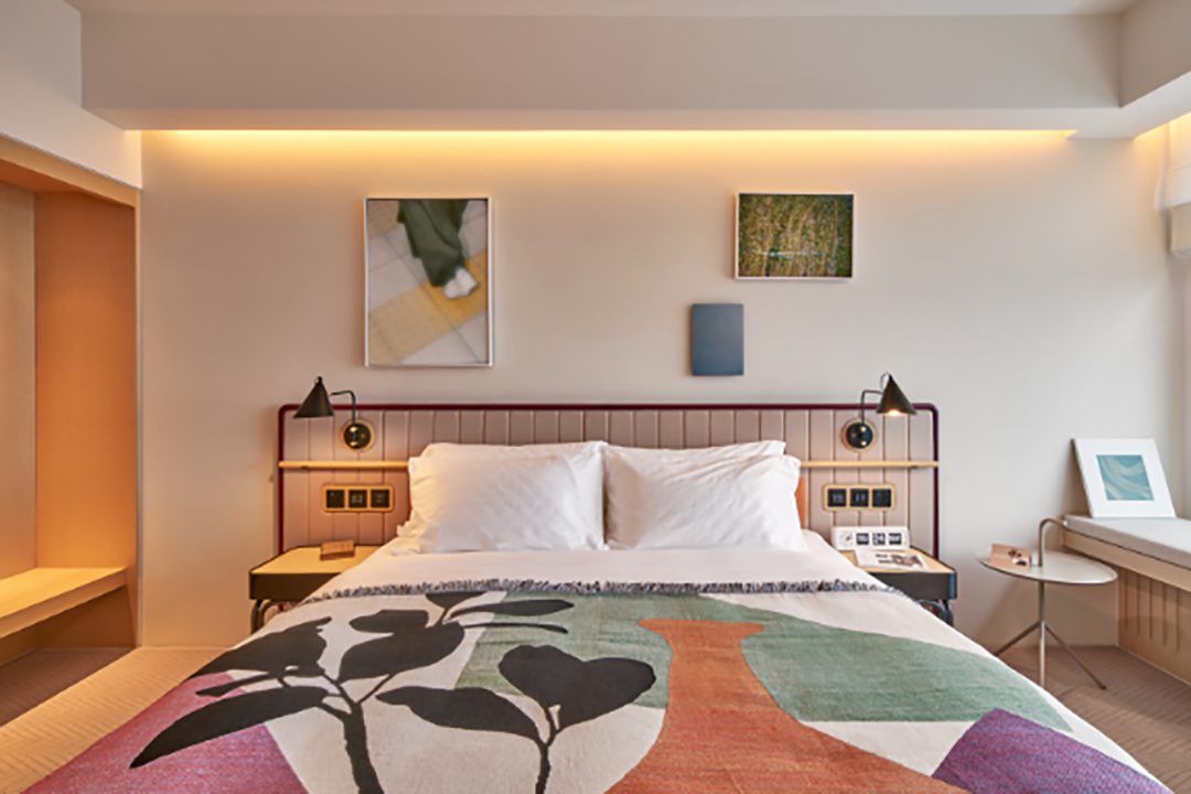 A modern hotel room featuring a bed with a colorful blanket, abstract art, and warm lighting.