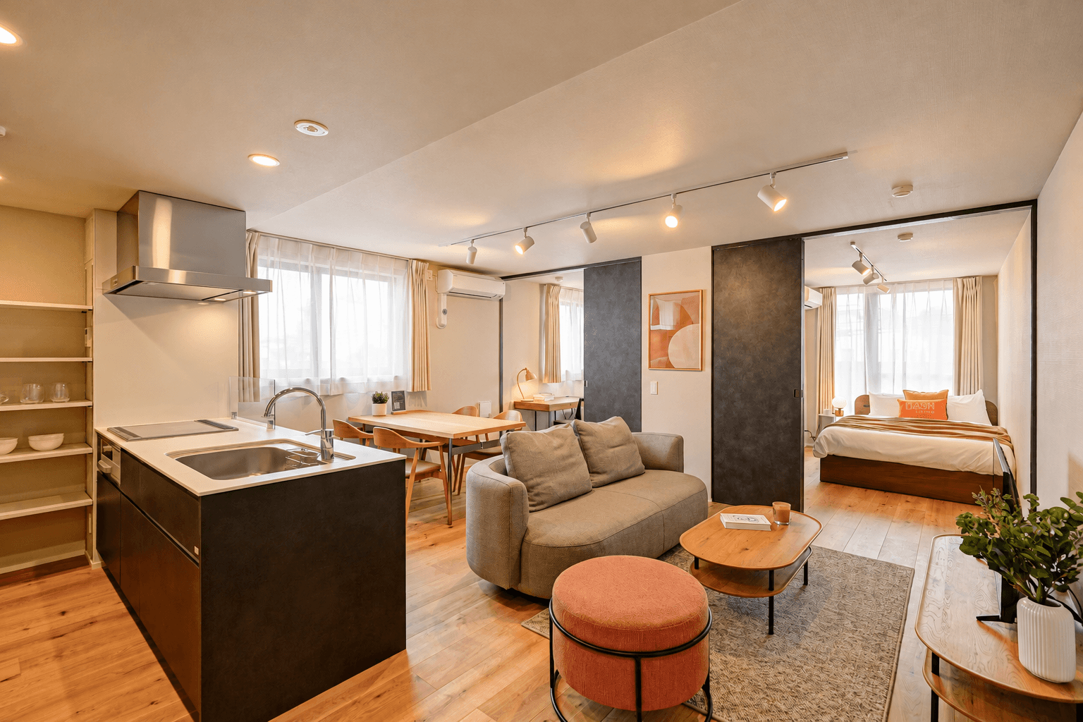 Modern open-plan apartment featuring a kitchen, living room with sofa, dining area, and visible bedroom.
