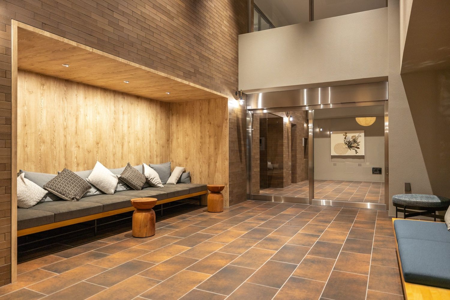 A modern lobby with a wooden alcove seating area, grey cushions, and tiled floor.