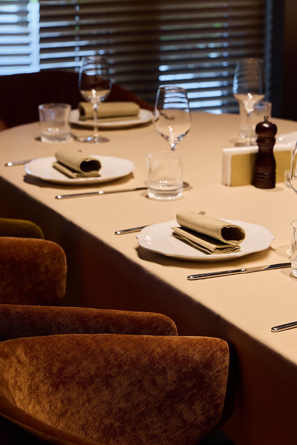 Elegant restaurant dining table set with white plates, glasses, and brown velvet chairs.