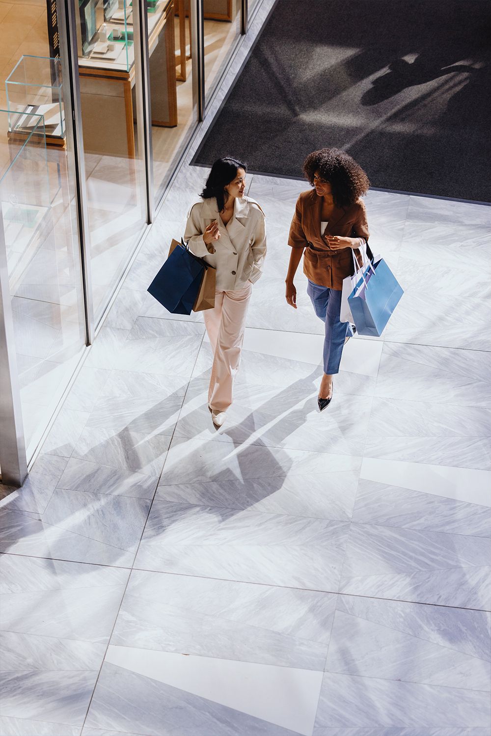 Two women walk away with shopping bags in a modern, brightly lit mall.