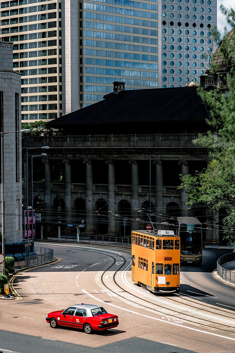 Yellow tram and red car on a city street with skyscrapers and a historic building.