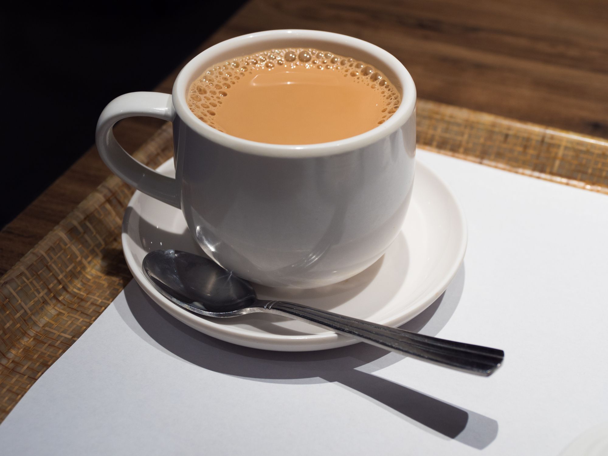 White mug filled with frothy chai tea on a matching saucer with a silver spoon.