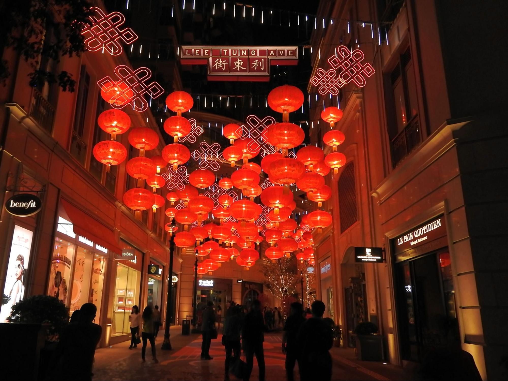 Red Chinese lanterns illuminate a bustling outdoor shopping street at night with people walking.