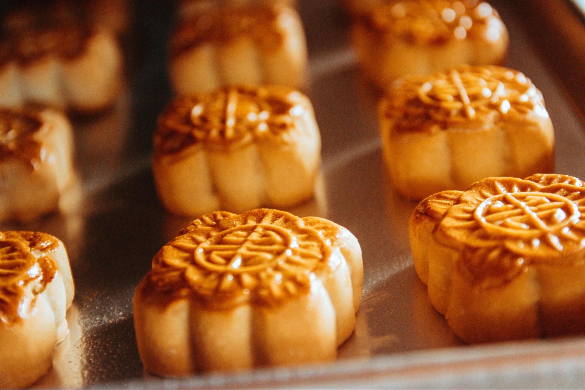 Golden brown mooncakes with intricate patterns baking on a silver tray.