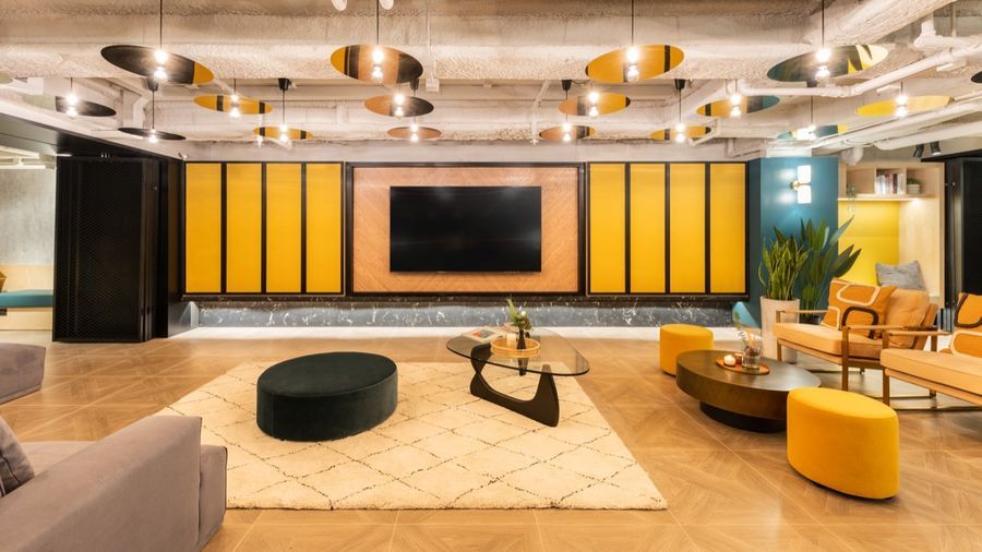 Modern lounge featuring a large TV, yellow paneling, unique lights, and contemporary seating.