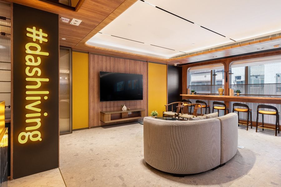Modern lounge area with a prominent #dashliving sign, curved sofa, and large television.
