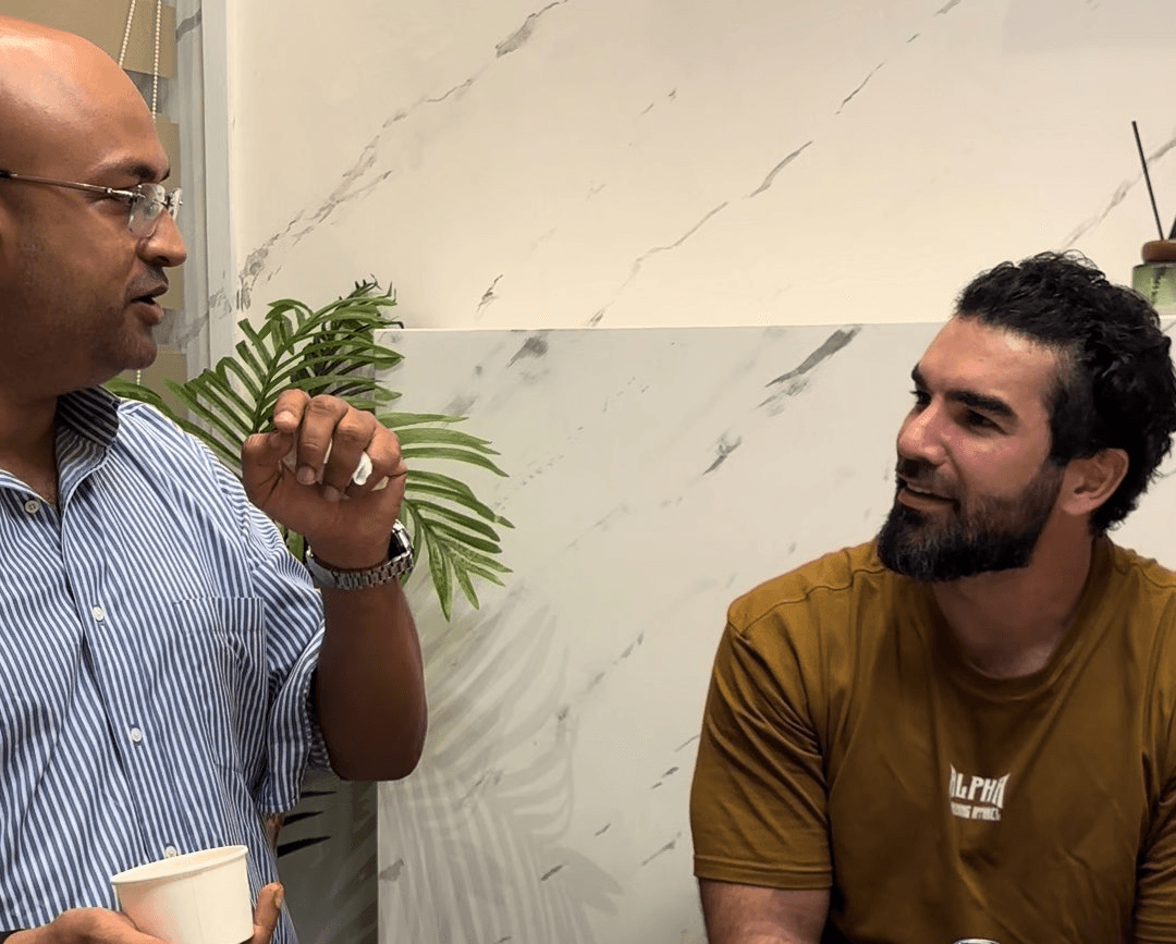Two men engaged in conversation, one gesturing while holding a cup.