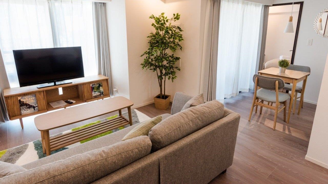 Modern living room with a gray sofa, TV, coffee table, and adjacent dining area.