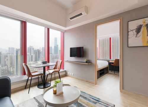 Modern apartment living room with city view, dining area, and glimpse of bedroom.