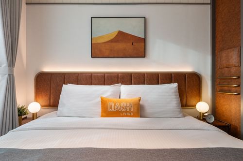 Modern bedroom with a bed, orange 'Enjoy Every Moment' pillow, and desert-themed art.