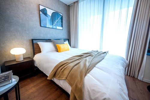A modern bedroom with a white bed, yellow pillow, beige throw, and a large bright window.