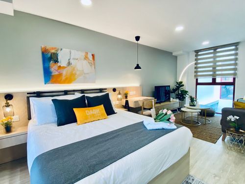 Modern hotel room with a large bed, abstract art, and a bright sitting area.