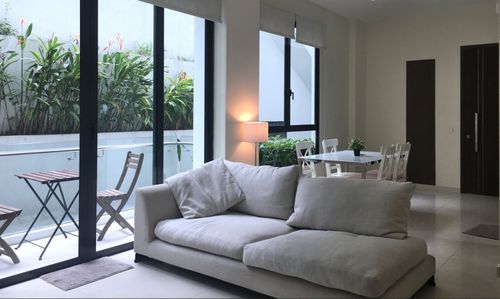 Modern living room with light sofa, dining area, and windows overlooking a green patio.