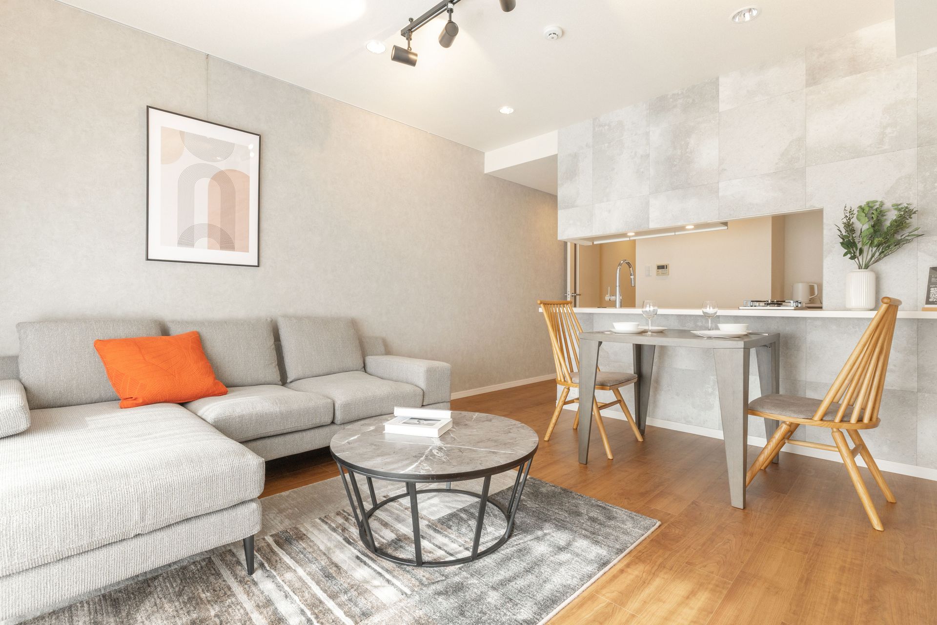 Modern living room with grey sofa, round marble coffee table, and adjacent dining area.