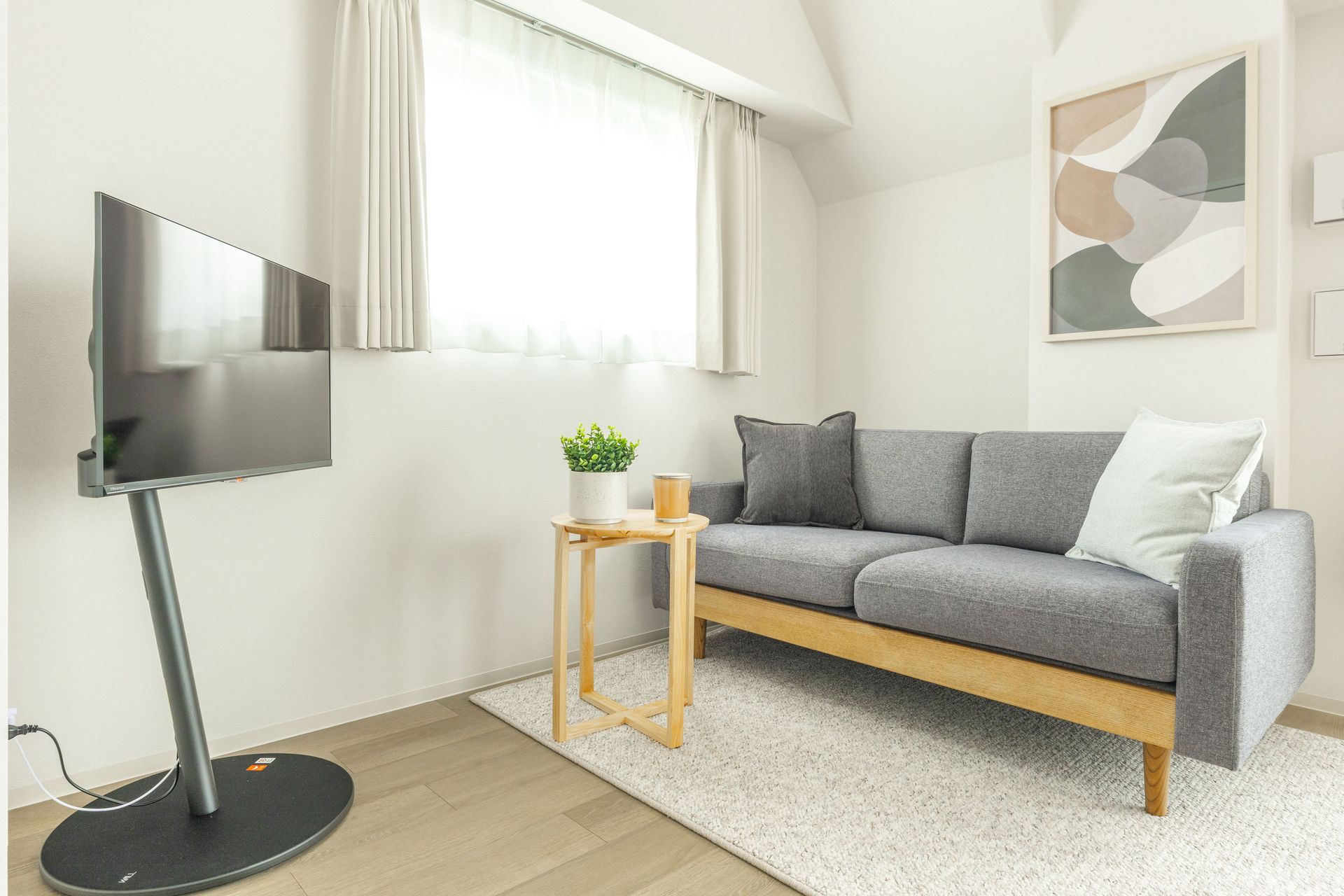 A minimalist living room featuring a grey sofa, modern TV, and abstract wall art.