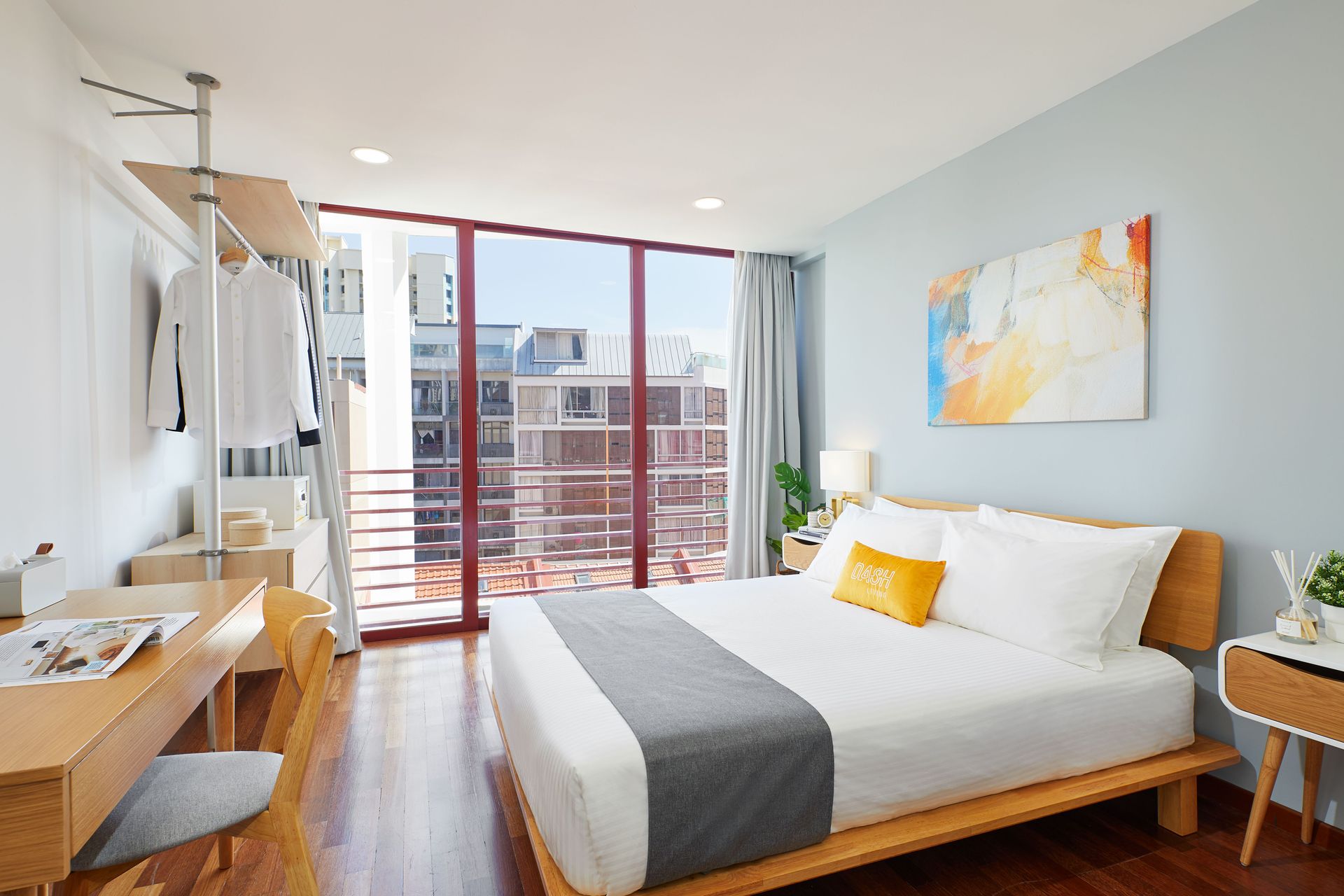 Bright, contemporary bedroom with a large bed, wooden desk, and city view window.