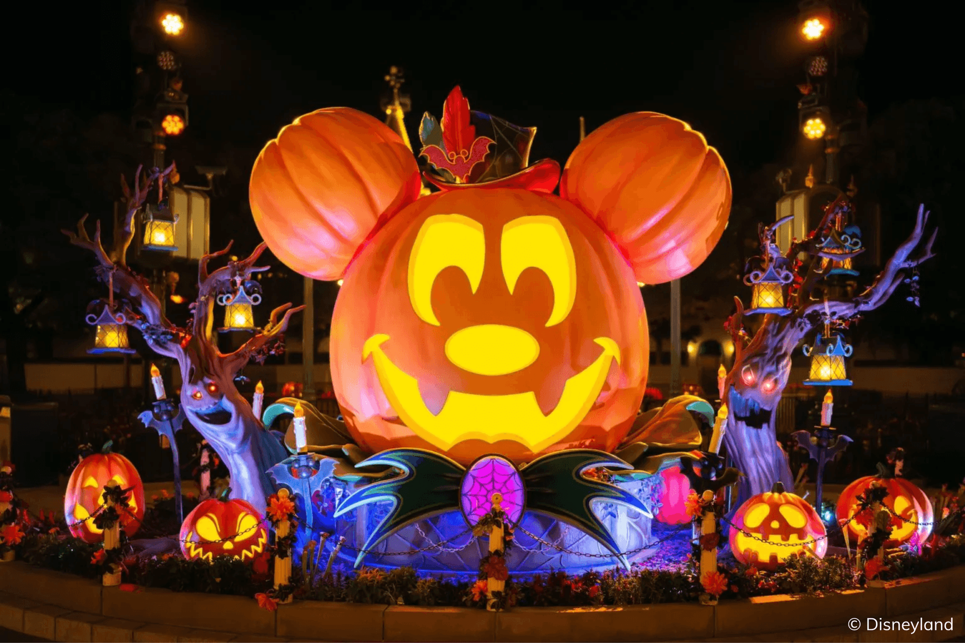 A giant, illuminated Mickey Mouse pumpkin is surrounded by Halloween decorations at night.