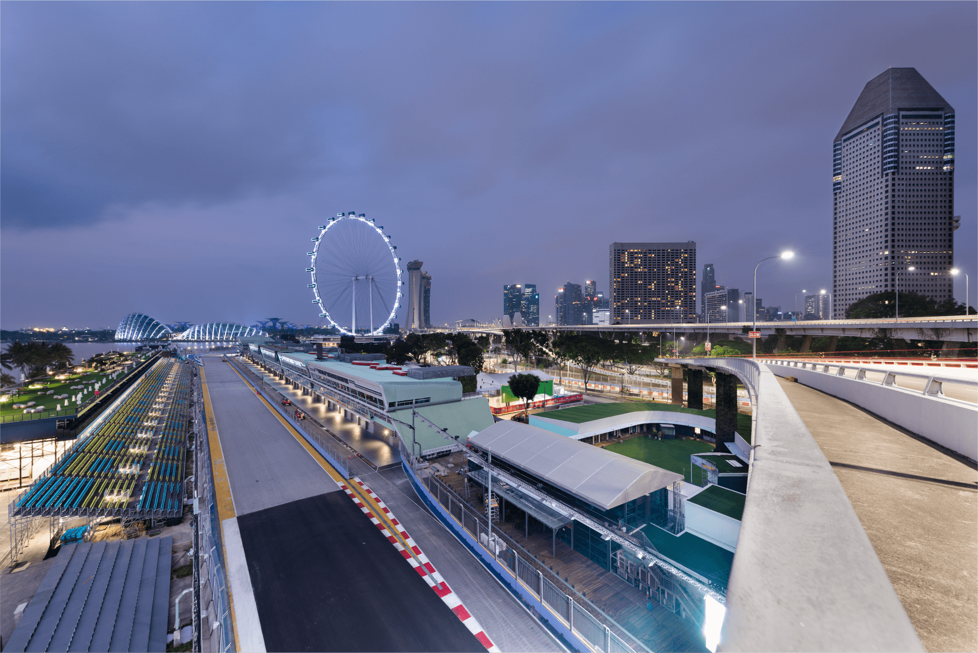 Singapore Formula 1 street circuit at twilight with city skyline and illuminated Ferris wheel.