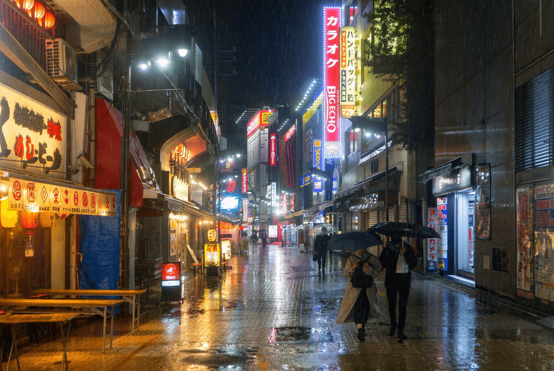 Rainy night in a vibrant Japanese city street with neon signs and people under umbrellas.
