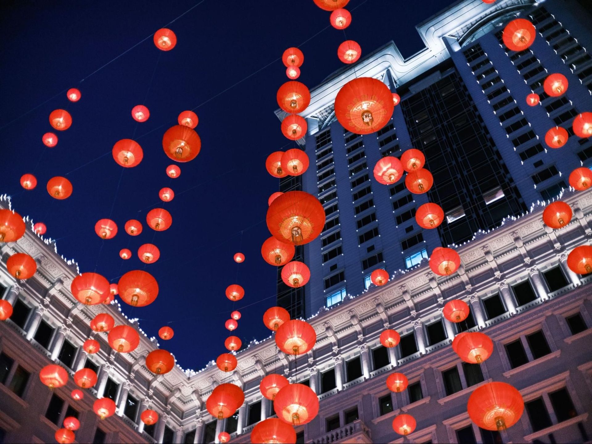 Red Chinese lanterns illuminate the night sky above city buildings.